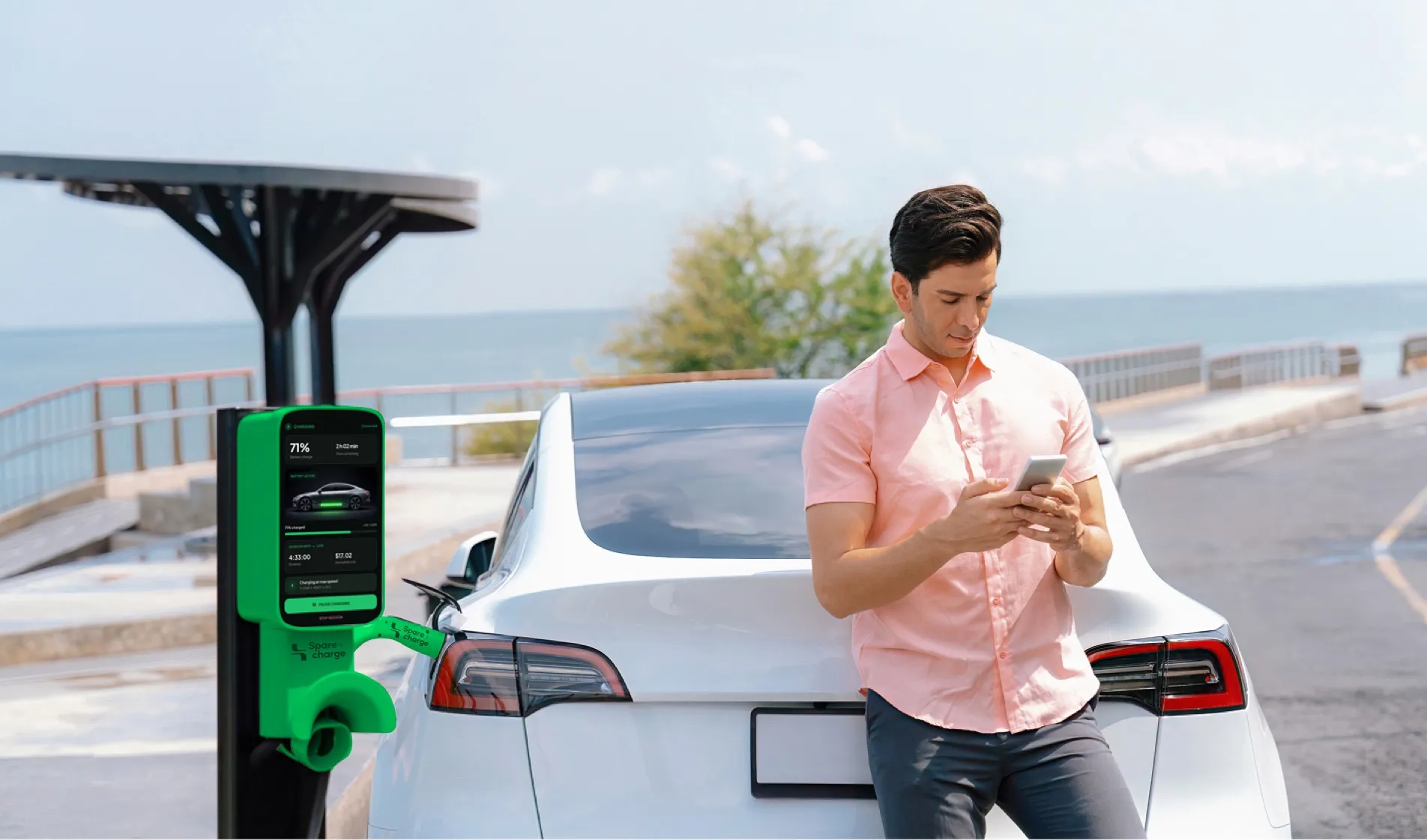 Man checking his phone beside his electric car at a seaside SpareCharge charger