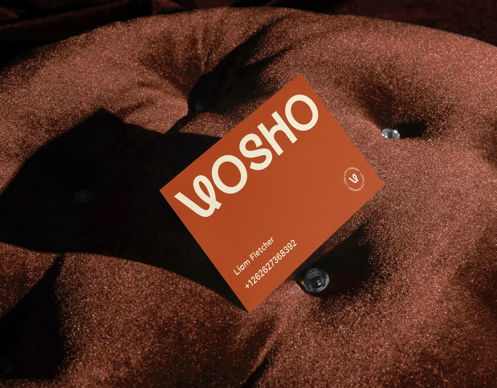 Orange Vosho business card on a rust brown tufted sofa