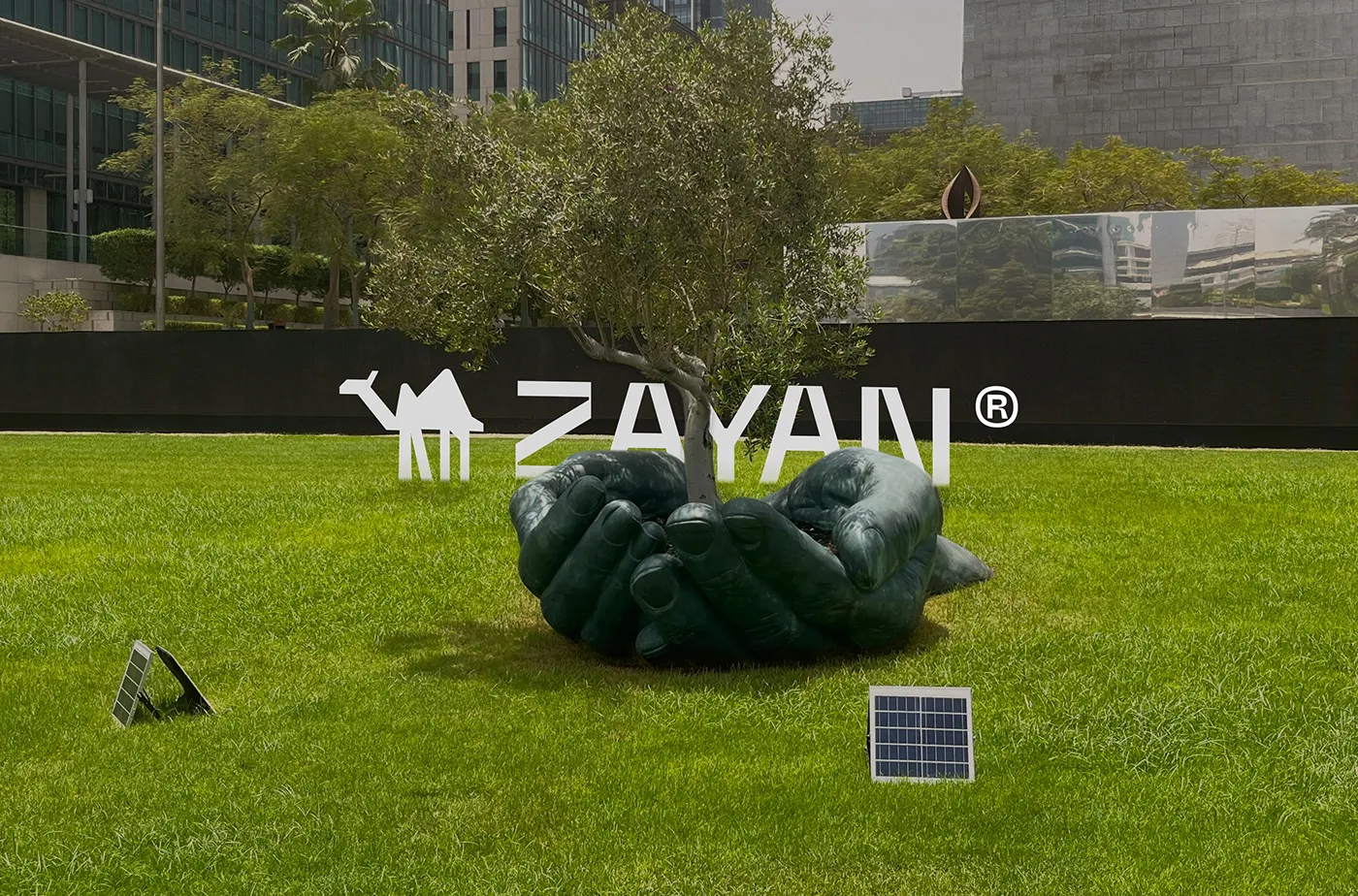 ZAYAN logo on a billboard above a park with a sculpture and a solar panel