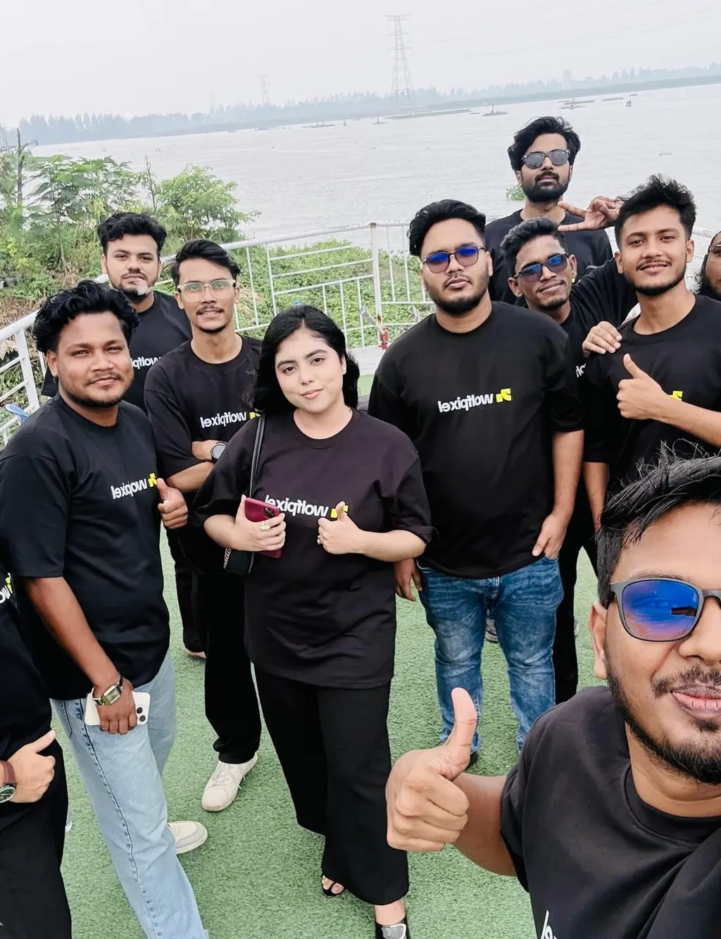 The team giving a thumbs-up on a riverside lawn