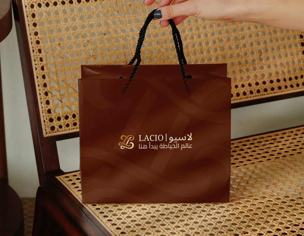 Brown Lacio shopping bag with the bilingual logo, held above a cane chair