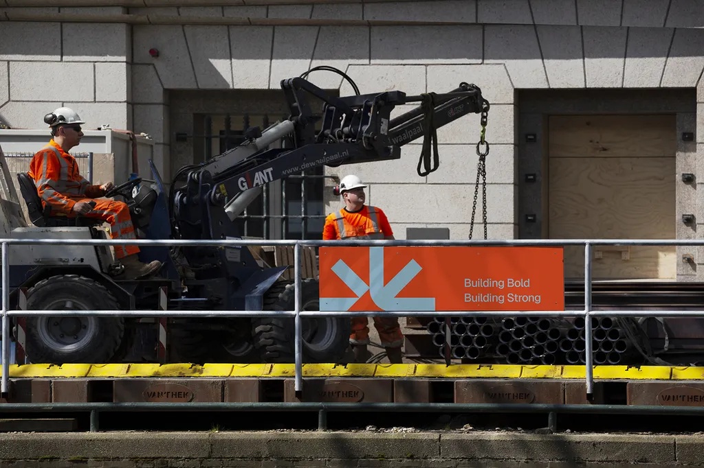 Site worker in orange hi-vis beside a machine with an Astrix Builders banner on the railing