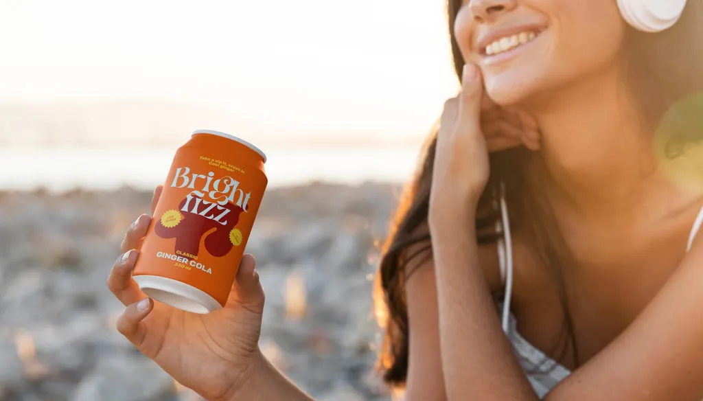 Smiling woman with headphones holding a Bright Fizz can by the sea