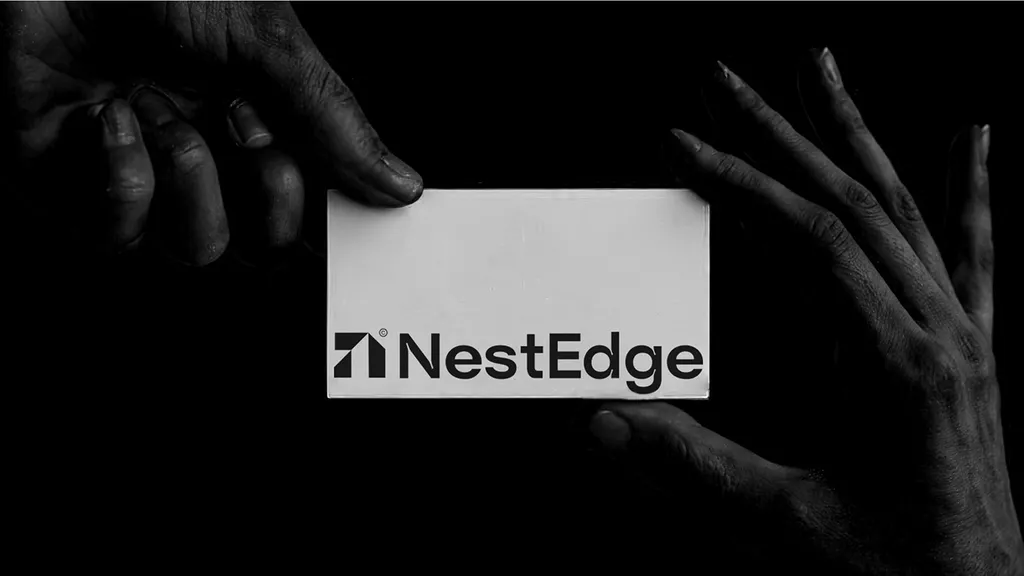 NestEdge business card with the black logo, held between two hands against a black background