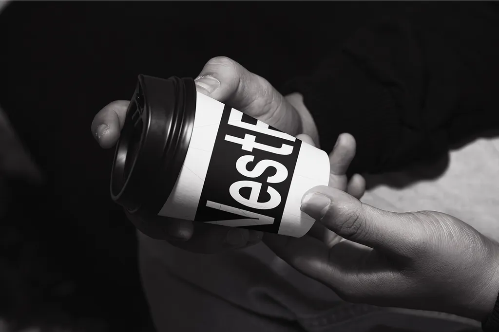 NestEdge coffee cup in black and white, held in two hands, with the wordmark wrapped around it