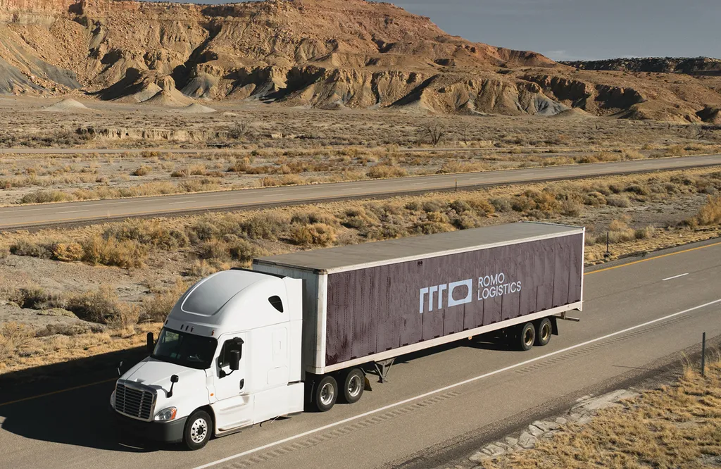 ROMO Logistics truck livery: a white truck pulling a brown ROMO trailer along a desert highway