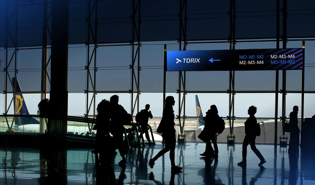 TORIX direction sign above travelers walking through an airport terminal in silhouette, with planes outside