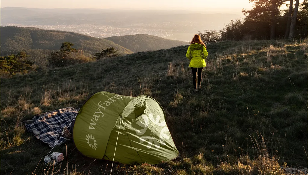Hiker walking up a hillside at sunset past a lime Wayfare tent