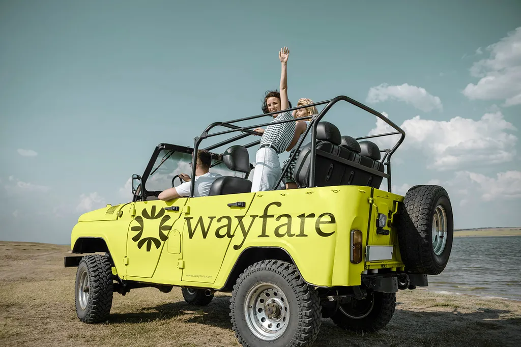Lime Wayfare jeep with the sun logo parked on a beach, a woman standing in the back