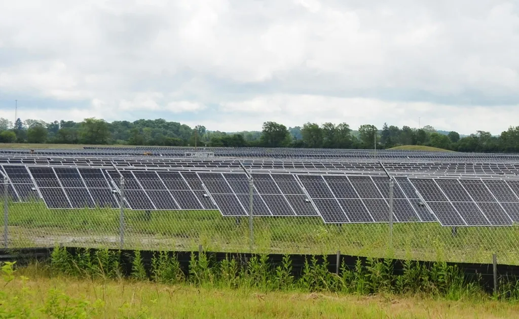 Rows of solar panels in a green field under a cloudy sky